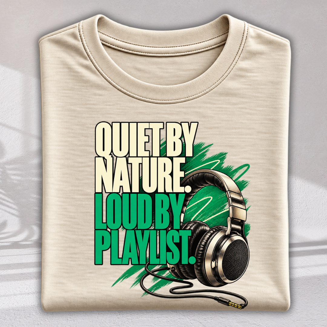 A folded beige crewneck t-shirt featuring a graphic print with the text 'QUIET BY NATURE LOUD BY PLAYLIST.' in cream and bright green, alongside a graphic of black and silver over-ear headphones on a gray background.