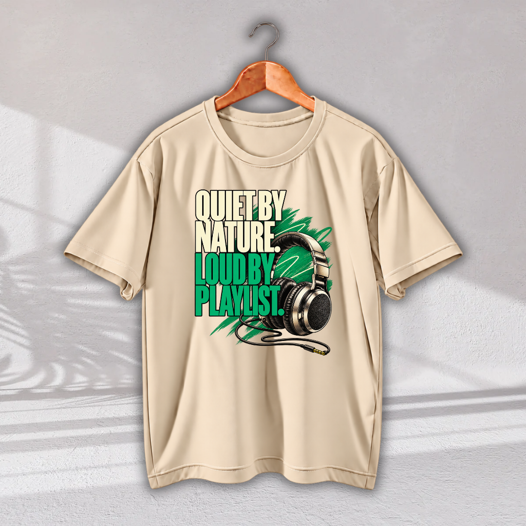 A beige short-sleeve crewneck t-shirt hanging on a wooden hanger against a textured gray wall. The shirt features a graphic print with the text 'QUIET BY NATURE, LOUD BY PLAYLIST.