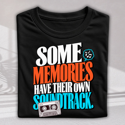 A folded black t-shirt with a colorful retro graphic that reads 'SOME MEMORIES HAVE THEIR OWN SOUNDTRACK.' in white, orange, and blue text, featuring a cassette tape illustration.