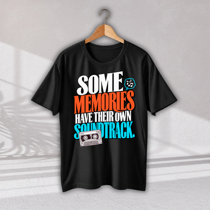 A black short-sleeve t-shirt hanging on a wooden hanger against a light gray wall. The shirt features a colorful retro graphic with the text 'SOME MEMORIES HAVE THEIR OWN SOUNDTRACK.